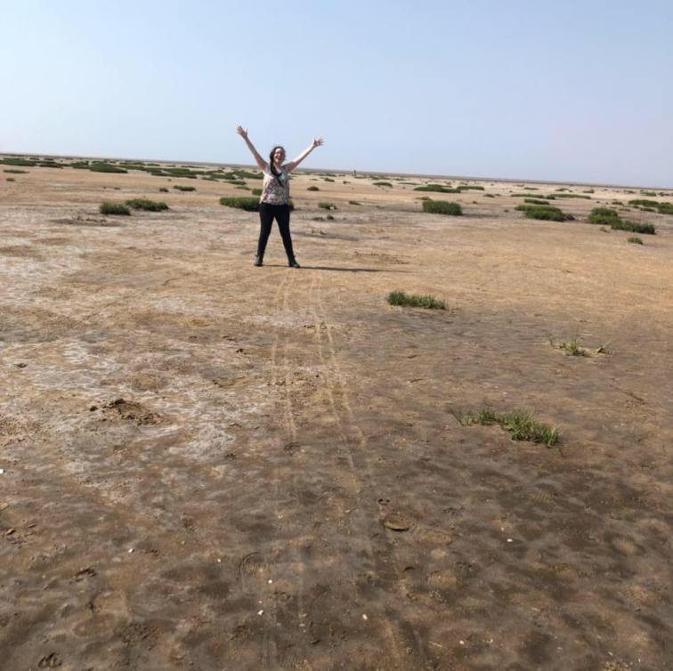Dark-haired woman on the beach at Southport, smiling and doing a silly pose